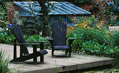 DECKING_BESIDE_LILY_POOL_WITH_ADIRONDACK_CHAIRS_AND_GREENHOUSE_IN_THE_BACKGROUND___DESIGNER_DUNCAN_H
