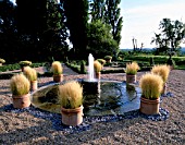 PARSONAGE  OMBERSLEY  WORCESTERSHIRE: PARTERRE ON OLD TENNIS COURT WITH TERRACOTTA CONTAINERS PLANTED WITH STIPA TENUISSIMA AROUND A WATER SPOUT