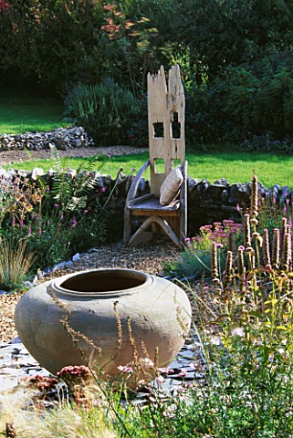 WOODEN_THRONE_CHAIR_IN_THE_GRAVEL_GARDEN_WITH_LARGE_URN_SITTING_ON_A_RAISED_BROKEN_SLATE_BORDER_CLAR