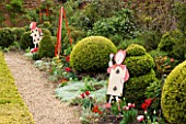 WEST GREEN HOUSE  HAMPSHIRE  SPRING. ALICE IN WONDERLAND CHARACTERS BESIDE BORDER WITH CLIPPED TOPIARY AND TULIPS
