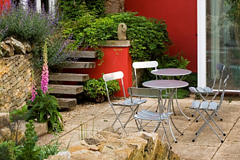 METAL_CHAIRS_SURROUND_CIRCULAR_TABLE_IN_FRONT_OF_RED_WALL_ON_PATIO_TERRACE_WINGWELL_NURSERY___RUTLAN