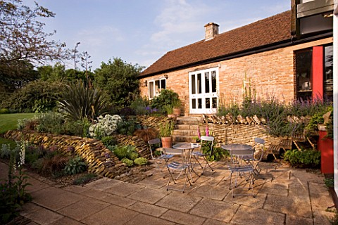 ANGLES_DRYSTONE_WALL__METAL_TABLE_AND_CHAIRS_ON_THE_PATIO_AT_THE_BACK_OF_THE_HOUSE_WINGWELL_NURSERY_