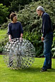 ROSE AND JOHN DEJARDIN ON THE LAWN WITH ALLIUM  A SCULPTURE BY RUTH MOILLIET. WINGWELL NURSERY   RUTLAND
