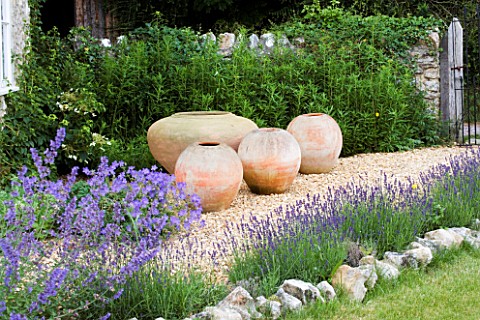 FOUR_TERRACOTTA_CONTAINERS_ON_A_GRAVEL_PATH_BESIDE_THE_HOUSE_CLARE_MATTHEWS_GARDEN__DEVON