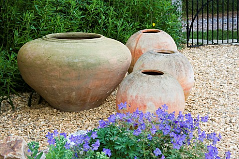 FOUR_TERRACOTTA_CONTAINERS_ON_A_GRAVEL_PATH_BESIDE_THE_HOUSE_CLARE_MATTHEWS_GARDEN__DEVON