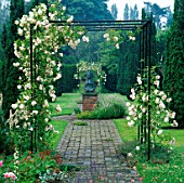 METAL ARBOUR WITH CLIMBING WHITE ROSE ADELAIDE DORLEANS OVER PATH AT LOWER HALL GARDEN  SHROPSHIRE. BRONZE SCULPTURE BY PETER BALL
