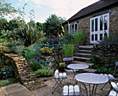 WINGWELL NURSERY  RUTLAND: PATIO AT THE BACK OF THE HOUSE WITH METAL CHAIRS AND TABLES. STONE WALLLS PLANTED WITH ACHILLEAS  PHORMIUM AND CRAMBE MARITIMA