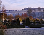 VIEW ACROSS PARTERRE TO OPEN COUNTRYSIDE WITH RIDGE AND FURROW FIELD  AT PETTIFERS IN  FROST.  TOPIARY