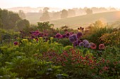PETTIFERS  OXFORDSHIRE: DAWN LIGHT ON BORDER PLANTED WITH ALLIUM PURPLE SENSATION AND ASTRANTIA ROMA WITH COUNTRYSIDE BEYOND