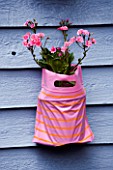 DESIGNER: CLARE MATTHEWS - PINK PLASTIC PARTY BAG ON BLUE FENCE PLANTED WITH PINK FLOWERS