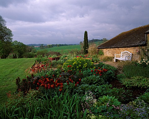 PETTIFERS__OXFORDSHIRE_SPRING_BORDER_AND_VIEW_TO_COUNTRYSIDE_BEYOND_TULIP_QUEEN_OF_SHEBA__WHITE_BENC