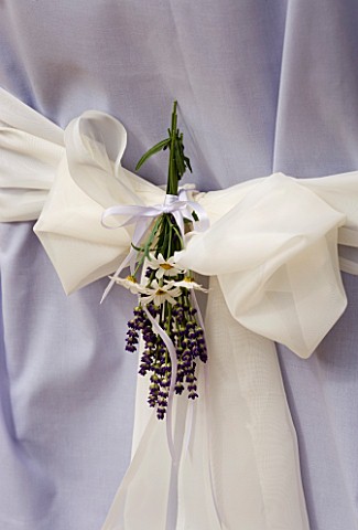 DESIGNER_CLARE_MATTHEWS_WHITE_BOW_BEHIND_SHEET_COVERED_CHAIR_WITH_BOUQUET_OF_LAVENDER_AND_DAISIES