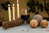 DESIGNER: CLARE MATTHEWS - DRIFTWOOD CANDLE PROJECT - CANDLE HOLDER AT NIGHT WITH GLASS OF WINE AND STONE BALLS ON TABLE