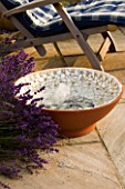 DESIGNER: CLARE MATTHEWS - BUBBLING BOWL PROJECT: TERRACOTTA WATER FEATURE ON PATIO BESIDE LAVENDER AND DECKCHAIR SHOWING GLASS BEADS AND WHITE MOSAIC