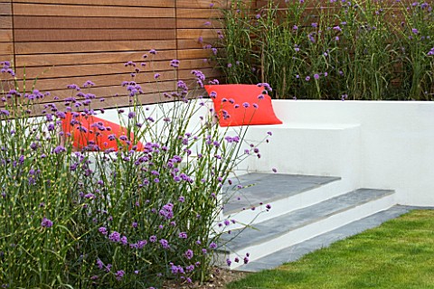 MINIMALIST_GARDEN_DESIGNED_BY_WYNNIATTHUSEY_CLARKE_RENDERED_WHITE_WALL_WITH_SEAT_AND_ORANGE_CUSHIONS