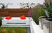 MINIMALIST GARDEN DESIGNED BY WYNNIATT-HUSEY CLARKE: RENDERED WHITE WALL WITH SEAT AND ORANGE CUSHIONS  VERBENA BONARIENSIS AND MISCANTHUS ZEBRINUS  AGAVE AMERICANA IN CONTAINER