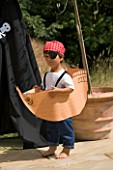DESIGNER CLARE MATTHEWS: CHILDRENS PARTY - BOY ON PATIO DRESSED AS A PIRATE AND IN A PAPER SHIP BESIDE BLACK PIRATE TENT