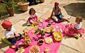 DESIGNER CLARE MATTHEWS: CHILDRENS PARTY - CHILDREN EATING PARTY FOOD OFF A PINK CLOTH ON THE PATIO - PICNIC
