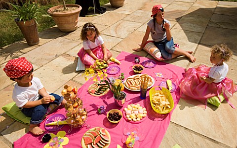 DESIGNER_CLARE_MATTHEWS_CHILDRENS_PARTY__CHILDREN_EATING_PARTY_FOOD_OFF_A_PINK_CLOTH_ON_THE_PATIO__P