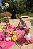 DESIGNER CLARE MATTHEWS: CHILDRENS PARTY - CHILDREN EATING PARTY FOOD OFF A PINK CLOTH ON THE PATIO - PICNIC
