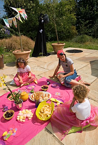 DESIGNER_CLARE_MATTHEWS_CHILDRENS_PARTY__CHILDREN_EATING_PARTY_FOOD_OFF_A_PINK_CLOTH_ON_THE_PATIO__P