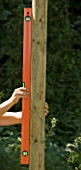 DESIGNER: CLARE MATTHEWS - TREEHOUSE PROJECT: USING SPIRIT LEVEL TO CHECK ON WOODEN UPRIGHT