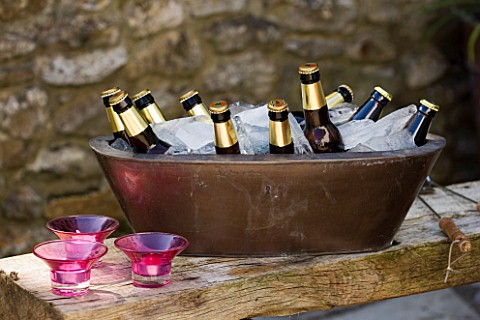 DESIGNER_CLARE_MATTHEWS__COPPER_CONTAINER_WITH_BEER_AND_ICE_ON_WOODEN_TABLE_WITH_CANDLES