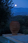 NIGHT VIEW ACROSS SWIMMING POOL TOWARDS TERRACOTTA URN WITH FULL MOON  IN GINA PRICES CORFU GARDEN.