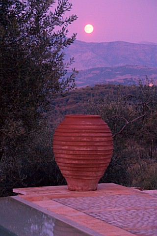 DUSK_VIEW_ACROSS_SWIMMING_POOL_TOWARDS_TERRACOTTA_URN_WITH_FULL_MOON__IN_GINA_PRICES_CORFU_GARDEN