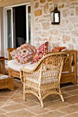 CANE CHAIR AND SOFA WITH LARGE INDIAN CUSHIONS ON PATIO. GINA PRICES CORFU GARDEN.