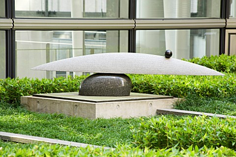 MARUNOUCHI_HOTEL__TOKYO__JAPAN_POLISHED_GRANITE_SCULPTURE_ON_STONE_PEDESTAL_WITH_OFFICE_BEHIND_ROOF_