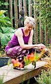 KATHY TAYLOR CROUCHES OVER POND IN DECKED AREA IN HER LONDON GARDEN