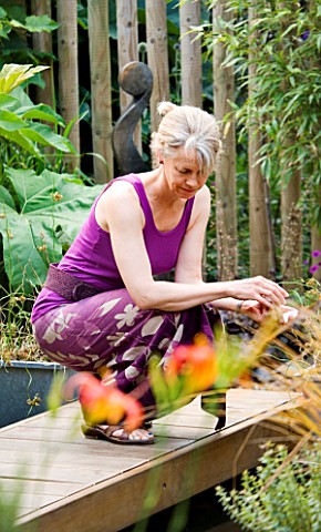 KATHY_TAYLOR_CROUCHES_OVER_POND_IN_DECKED_AREA_IN_HER_LONDON_GARDEN