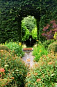 VEDDW HOUSE GARDEN  GWENT  WALES: DESIGNERS ANNE WAREHAM AND CHARLES HAWES - VIEW THOUGH HORNBEAM TUNNEL TO CUT OUT DOVE SCULPTURE WITH BIRD BATH IN THE FOREGROUND
