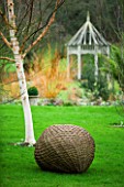 WOODPECKERS  WARWICKSHIRE  WINTER: WOVEN WILLOW BALL SCULPTURE IN LAWN WITH BETULA HERGEST AND SUMMERHOUSE