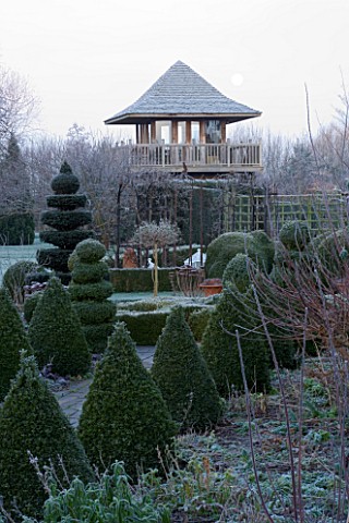 WOODPECKERS__WARWICKSHIRE__WINTER_THE_FORMAL_TOPIARY_GARDEN_IN_FROST_WITH_SUMMERHOUSE_TOWER_BEHIND
