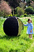 DESIGNER: DAVID HARBER. GARDEN DESIGNED BY ANGEL COLLINS - PEBBLE SPHERE IN WILDFLOWER MEADOW WITH GIRL STANDING NEARBY