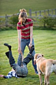 GIRL AND BOY PLAYING IN GARDEN WITH DOG WATCHING ON