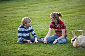 GIRL (AGED 15) AND BOY (AGED 12) SITTING IN A GARDEN AND LAUGHING  WITH DOG. FUN  ENJOYING  ENJOYMENT