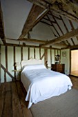 BOONSHILL FARM  EAST SUSSEX. INTERIOR OF BEDROOM WITH WOODEN FLOORBOARDS  EXPOSED BEAMS AND BED WITH FRENCH WOODEN HEADBOARD. DESIGNER: LISETTE PLEASANCE