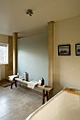 BOONSHILL FARM  EAST SUSSEX. INTERIOR OF BATHROOM WITH BATH AND WOODEN BENCH WITH MOTHER OF PEARL INLAY FROM INDIA. FRAMED PHOTOGRAPHS BY MICK SHAW. DESIGNER: LISETTE PLEASANCE