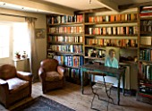 BOONSHILL FARM  EAST SUSSEX. INTERIOR OF STUDY WITH BOOKSHELVES MADE FROM RECLAIMED JOISTS MADE BY MICK SHAW. OLD LEATHER ARMCHAIRS AND OLD WOODEN DESK & CHAIR D: LISETTE PLEASANCE