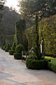 HOLKER HALL  CUMBRIA - THE SUNKEN GARDEN AT DUSK WITH BOX HEDGING  WOODEN BENCH  SEAT  AND STATUARY. FORMAL GARDEN