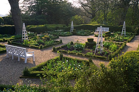 KELMARSH_HALL__NORTHAMPTONSHIRE_FORMAL_GARDEN_IN_WOODLAND_IN_SPRING_WITH_WHITE_BENCHES_AND_TRIPODS