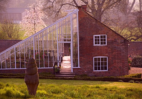 KELMARSH_HALL__NORTHAMPTONSHIRE_THE_GREENHOUSE_IN_THE_WALLED_GARDEN_AT_DUSK_IN_THE_SPRING_WITH_WOODE