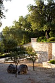 CORFU  GREECE: VILLA ZOGRAFIA  NORTH EAST CORFU. DESIGN BY ALITHEA JOHNS OF SKOPOS DESIGN AND RAHDY ELWAN. COURTYARD WITH ROCKS AND TREES  STONE WALL AND OLIVE TREES