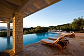 CORFU  GREECE: VILLA IN NORTH EAST CORFU. DESIGN BY ALITHEA JOHNS OF SKOPOS DESIGN AND RAHDY ELWAN. RECTANGULAR INFINITY SWIMMING POOL WITH SUN LOUNGERS AND COVERED CANOPY