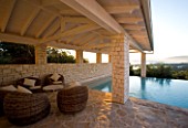 CORFU  GREECE: VILLA IN NORTH EAST CORFU. DESIGN BY ALITHEA JOHNS OF SKOPOS DESIGN AND RAHDY ELWAN. RECTANGULAR INFINITY SWIMMING POOL AT DAWN WITH WICKER SEATS AND COVERED CANOPY