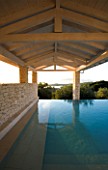 CORFU  GREECE: VILLA IN NORTH EAST CORFU. DESIGN BY ALITHEA JOHNS OF SKOPOS DESIGN AND RAHDY ELWAN. RECTANGULAR INFINITY SWIMMING POOL AT DAWN WITH COVERED CANOPY