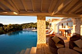 CORFU  GREECE: VILLA IN NORTH EAST CORFU. DESIGN BY ALITHEA JOHNS OF SKOPOS DESIGN AND RAHDY ELWAN. RECTANGULAR INFINITY SWIMMING POOL AT DAWN WITH WICKER SEATS AND COVERED CANOPY